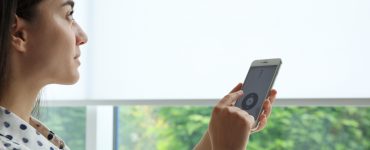 Woman using smart home application on phone to control window blinds indoors