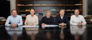 five men sitting at desk with paperwork